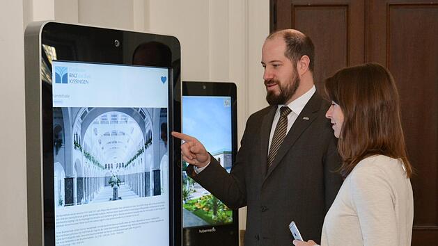 Timo Tully (Leiter der Abteilung Gästeservice der Bayerischen Staatsbad Bad Kissingen GmbH) und Kathrin Betzen (Leiterin der Marketingabteilung der Bayer. Staatsbad Bad Kissingen GmbH) probieren das neue elektronische Informationssystem aus. Darin enthaltene Informationen können per QR-Code leicht auf das eigene Mobilfunkgerät übertragen werden. Björn Hein