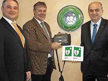 Leicht zugänglich ist der Defibrillator, der im Notfall Leben retten kann. Bürgermeister Gerhard Wunder (M.) informiert sich über die Handhabung, Thomas Kolb (r.) zeigt das Hinweisschild, das außen an der Bank angebracht wird. Links Geschäftsstellenleiter Jens Kremer. Foto: Deuerling