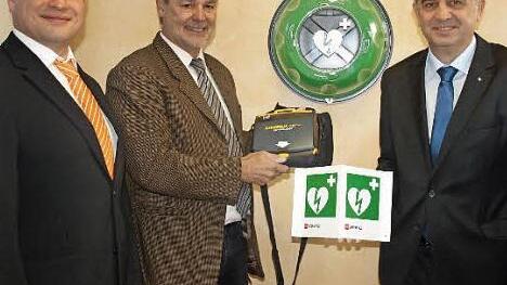 Leicht zugänglich ist der Defibrillator, der im Notfall Leben retten kann. Bürgermeister Gerhard Wunder (M.) informiert sich über die Handhabung, Thomas Kolb (r.) zeigt das Hinweisschild, das außen an der Bank angebracht wird. Links Geschäftsstellenleiter Jens Kremer. Foto: Deuerling