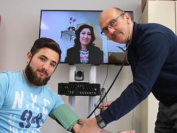 Einfaches Prinzip: Während Dr. Nagham Soda (hinten) über einen Bildschirm von Bad Neustadt aus mit dem Patienten in Bad Kissingen spricht, kann ein Mitarbeiter des Roten Kreuzes Hilfestellungen geben und die Behandlungsempfehlungen notieren. Asylbewerber Mohammed Ali Tato (links) und Uve Bartz vom Roten Kreuz haben bei der Vorstellung des Pilotprojektes eine solche Szene nachgestellt. Foto: Ralf Ruppert