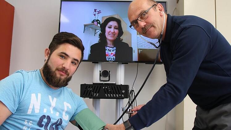 Einfaches Prinzip: Während Dr. Nagham Soda (hinten) über einen Bildschirm von Bad Neustadt aus mit dem Patienten in Bad Kissingen spricht, kann ein Mitarbeiter des Roten Kreuzes Hilfestellungen geben und die Behandlungsempfehlungen notieren. Asylbewerber Mohammed Ali Tato (links) und Uve Bartz vom Roten Kreuz haben bei der Vorstellung des Pilotprojektes eine solche Szene nachgestellt. Foto: Ralf Ruppert
