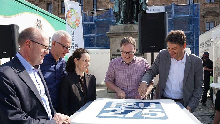Es ist gar nicht so einfach, so einen großen Kuchen in gleichmäßige Stücke zu zerteilen - Ob Florian Janik (Mitte) und der Präsident der Uni, Joachim Hornegger, stecken ordentlich Spott von den Vertretern der Jubiläumspartner (links im Bild) ein.