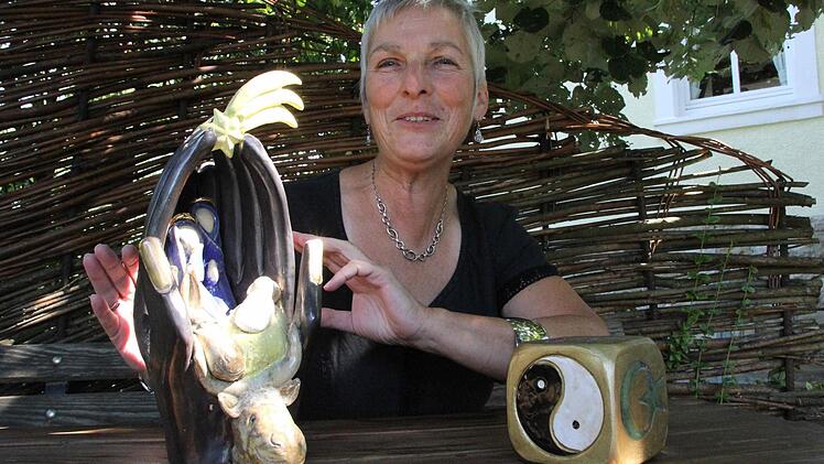 Das Fertigen von Urnen ist eine Ausnahme. Hier interpretiert die Künstlerin Barbara Gröhling zwei ihrer "normalen" Kunstwerke: links eine ungewöhnliche Krippe mit Wänden aus gefalteten Händen, rechts einen Würfel mit den Symbolen der sechs großen Weltreligionen.  Foto: Katja Kölbl