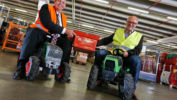 Vertriebsdirektor Christoph Serini (links) und Logistikdirektor Siegfried Gößwein haben auf Spielzeugtraktoren Platz genommen. Auch so etwas hat der Großhändler Kramp im Angebot. Von Bedeutung in der Strullendorfer Logistikzentrale sind aber Ersatzteile für die großen Maschinen. Foto: Matthias Hoch
