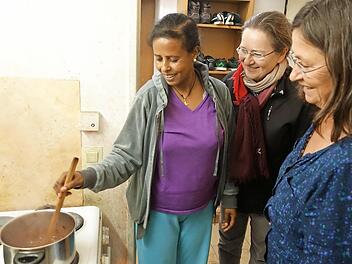 Angelockt vom leckeren Duft schauten bei der Spendenübergabe Pfarrgemeinderatsvorsitzende Ulrike Jira (Mitte) und die Caritas-Flüchtlingsbeauftragte Uschi Hartmann bei Sarim Gebremeskel vorbei, die gerade in der Gemeinschaftsküche ihr Essen zubereitete. Foto: Heike Beudert