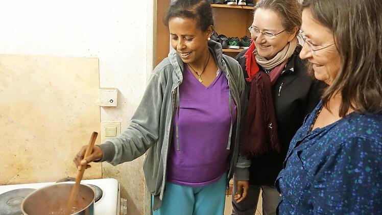Angelockt vom leckeren Duft schauten bei der Spendenübergabe Pfarrgemeinderatsvorsitzende Ulrike Jira (Mitte) und die Caritas-Flüchtlingsbeauftragte Uschi Hartmann bei Sarim Gebremeskel vorbei, die gerade in der Gemeinschaftsküche ihr Essen zubereitete. Foto: Heike Beudert