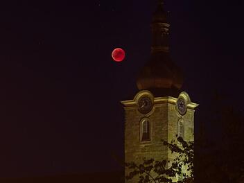 Leuchtend roter Ball vor dem illuminierten Kirchturm: Blutmond über der Stadtpfarrkirche in Ebern Foto: Jule Müller