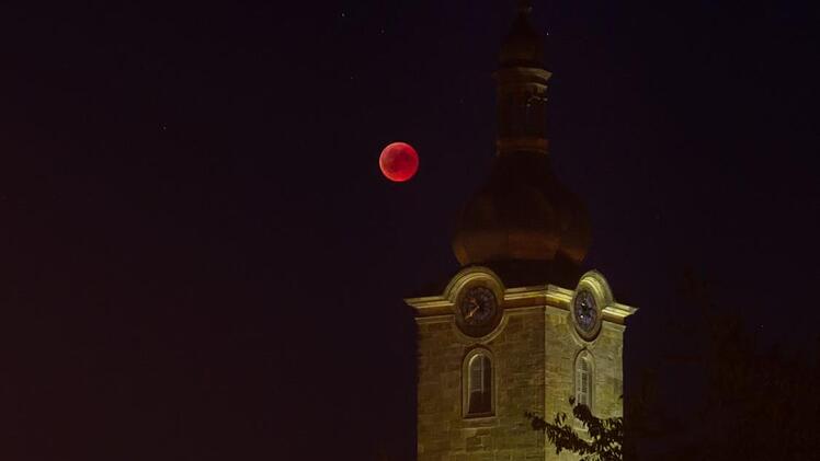 Leuchtend roter Ball vor dem illuminierten Kirchturm: Blutmond über der Stadtpfarrkirche in Ebern Foto: Jule Müller