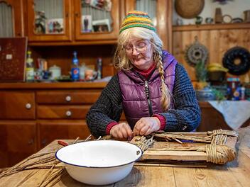 Das Arbeitszimmer dient auch als Wohnraum und als Küche. Hier flicht Helga Prommer ihre Korbwaren. Dazu gehören auch Reparaturarbeiten. Aktuell ist sie damit beschäftigt, die Sitzfläche eines Stuhls aus Binsen zu fertigen.  Foto: Klaus Gagel