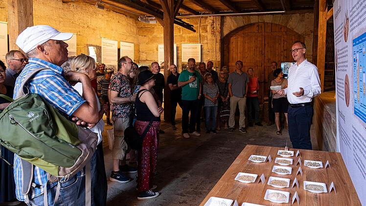 Andreas Hubmann (r.) stellt Besuchern das neu er&ouml;ffnete Scheunenmuseum der Minderleinsm&uuml;hle vor. Die Ausstellung zeigt historische Dokumente vom traditionellen Handwerksbetrieb zum modernen Bio-Unternehmen.