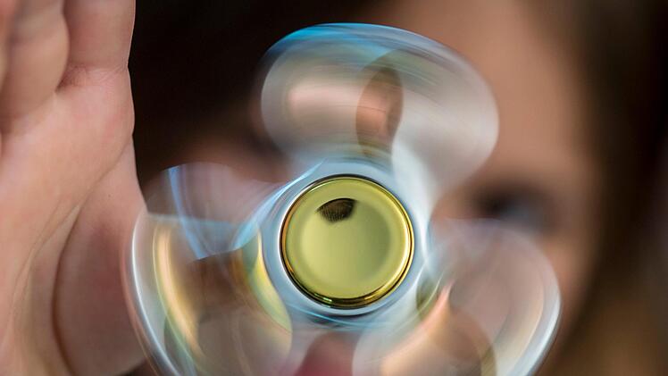 Ein Kind spielt mit einem Fidget-Spinner. Der flache Drehkreisel wird inzwischen so oft verkauft, dass der Handel Lieferschwierigkeiten hat. Foto: Boris Rößler/ dpa