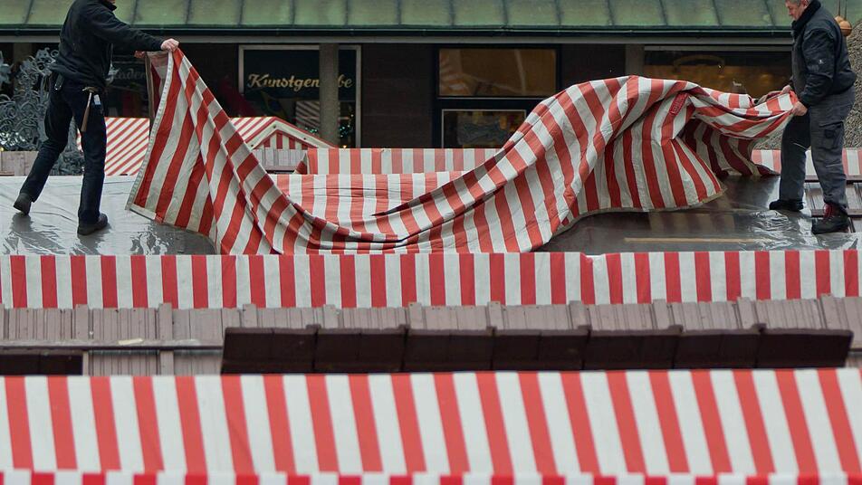 Zwei Männer montieren in Nürnberg die Dachplane an einem Verkaufsstand auf dem Christkindlesmarkt. Am 29. November wird der Markt offiziell mit dem Prolog des Nürnberger Christkinds eröffnet. Foto: Daniel Karmann/dpa