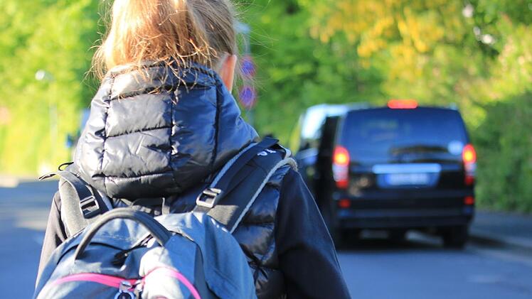 Ein  Mädchen läuft morgens die Stögerstraße entlang zur Sinnberg-Grundschule. Rechts  im Bild hält ein Elterntaxi im Kreuzungsbereich im absoluten Halteverbot,   um Kinder aussteigen zu lassen. Benedikt Borst