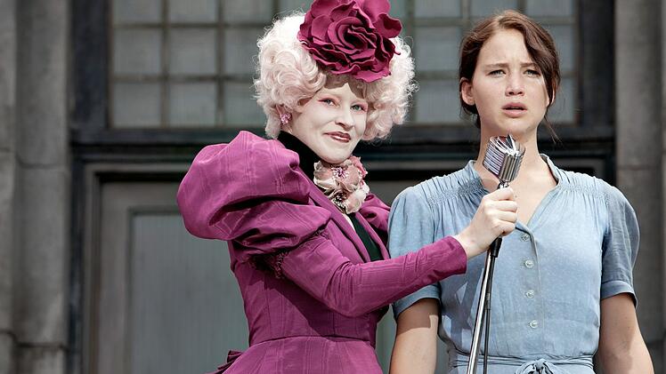 Als ihre kleine Schwester dazu auserkoren wird, an den blutigen Hungerspielen teilzunehmen, meldet sich Katniss (Jennifer Lawrence, rechts) freiwillig, um an ihrer Stelle in den Kampf zu ziehen. Die PR-Beauftragte (Elizabeth Banks) ist h&ouml;chst erfreut.