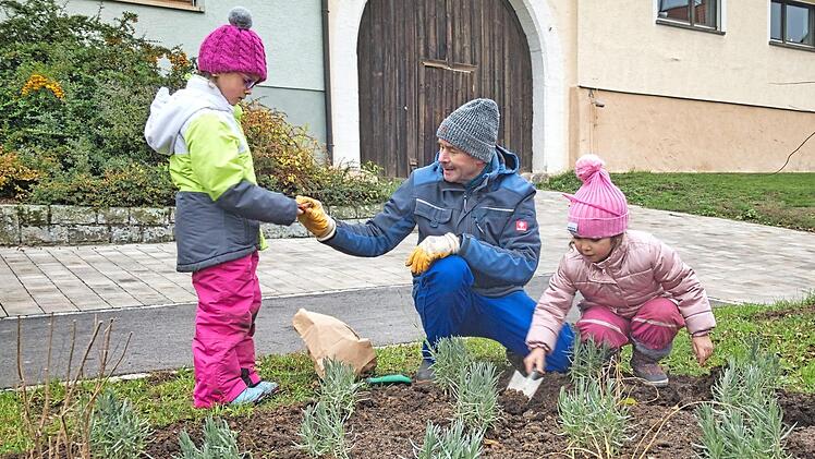 Roland Simon verteilte Blumenzwiebeln an Lotta, während Siham begeistert Pflanzlöcher gräbt. Zu Werke gingen die drei Gärtner im Blumenbeet vor dem Rathaus in Stettfeld.  Foto: Christian Ziegler