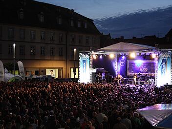 Ein lebhaftes Blues- & Jazzfestival bei Nacht in Bamberg. Eine große Menschenmenge genießt Live-Musik auf einer beleuchteten Bühne. Banner und Lichter schaffen eine feierliche Atmosphäre.