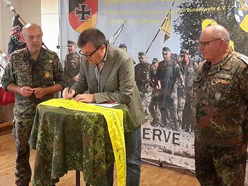 Riedenbergs Bürgermeister Roland Römmelt unterschreibt auf dem gelben Band. Die zwei Meter lange Banderole wird später symbolisch einer Einheit übergeben, die in den Auslandseinsatz geht. Interessierte Beobachter sind die Reservisten Johann Schmidt (links) und Karl Veit (rechts).Foto: Rolf Pralle