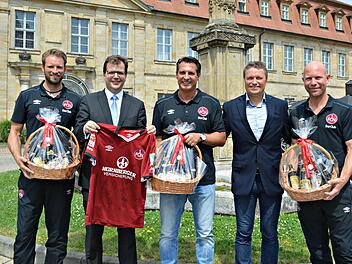Mit einem von den Spielern signierten Trikot revanchierten sich Coach Alois Schwarz (Mitte) und seine Co-Trainer bei B&uuml;rgermeister Christian Lange f&uuml;r das Bamberger Biergeschenk. Foto: Stadt Bamberg, Pressestelle