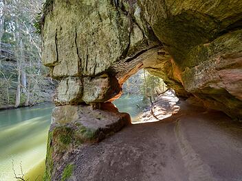 Die Schwarzachschlucht bietet mit ihren bizarren Felsformationen, moosbewachsenen Höhlen und der idyllischen Landschaft am Kanalufer eine wildromantische Kulisse für Wanderer. Der Rundweg durch das schluchtartige Flusstal, das sich über etwa 2,2 Kilometer erstreckt, befindet sich südlich von Schwarzenbruck im Landkreis Nürnberger Land in Mittelfranken, Bayern. Benannt nach dem Fluss Schwarzach, markiert die Schlucht die südliche Grenze des Lorenzer Reichswaldes. Die Schwarzach selbst bildet hier die Grenze zwischen dem nördlich gelegenen Landkreis Nürnberger Land und dem Landkreis Roth.