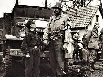 Links: Die Aufnahme  vom April 1945 erinnert an die kurze Zeit der "Werwölfe" aus dem Landkreis Kronach und  entstand nach der Gefangennahme der Nachwuchssoldaten. Ein amerikanischer Militärpolizist der 11. Armed Division hält dem damals 15-jährigen Philipp Reißenweber (Gemeinde Stockheim) die Hand. Der Schnappschuss. Rechts: Die Uniformverbrennung vor dem  alten Kronacher Rathaus nutzten die Amerikaner zu Propagandazwecken in den USA.Repros: Gerd Fleischmann