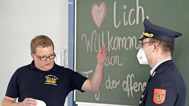 Wie kleiden sich Feuerwehrleute? Gruppenf&uuml;hrer Stephan Ludwig (links) erkl&auml;rt es den Zuschauern im Livestream mit Hilfe der Uniform von Stadtbrandinspektor Florian H&ouml;fner.