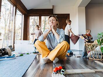 Frustrierende Frau allein kämpft Burnout mit Kindern. Gestresste Mutter sitzt auf dem Boden in der Mitte des Spielzeugs, während die Kinder frech um sie herum im Zimmer laufen. Familie zu Hause mit Chaos, Unordnung. Alleinerziehend, Stress, Kinder.Frustrating woman alone struggling burnout with kids. Stressed out mother sitting on floor in middle of toys while children naughty running around her at room. Family home with chaos, mess.