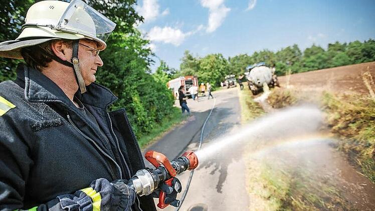 Ein Kronacher Wehrmann spritzt Wasser auf den Rand des abgebrannten Feldes. Zu sehen ist, dass ringsherum Wald verläuft.  Fotos: Steffens