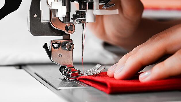 Hände einer Frau auf rotem Stoff mit Nähmaschine. Selbstgemachte Kleidung Konzept. Hobby-Konzept. Kleidung reparieren Konzept.