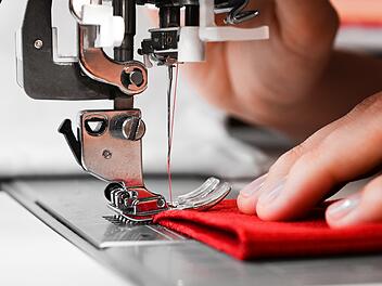 Hände einer Frau auf rotem Stoff mit Nähmaschine. Selbstgemachte Kleidung Konzept. Hobby-Konzept. Kleidung reparieren Konzept.