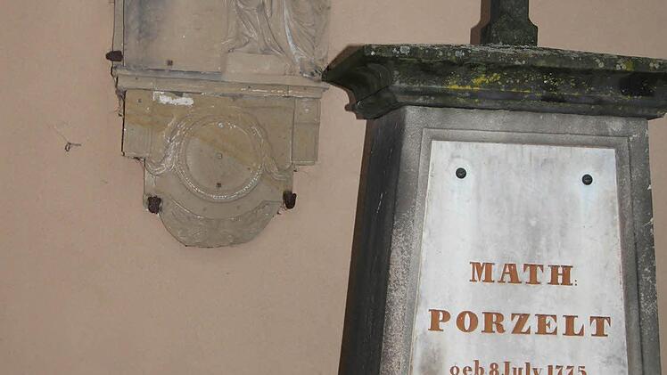 Der Grabsteinrest an der Wand zeigt eine trauernde Frau, die an eine Säule gelehnt ist - er wurde an die Wand montiert, als Erinnerung an einen besonders kunstvollen Grabstein.