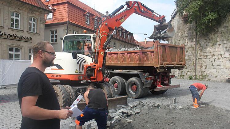 Frank Rauh (links) ist mit dem Baufortschritt zufrieden. Im Hintergrund belädt ein Bagger einen Lastwagen mit Steinen. Dazu nutzt er einen Sieblöffel, durch den der Split beim Anheben herausfallen kann.