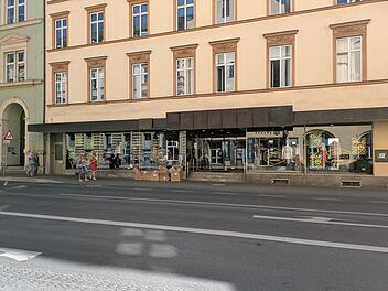 Die Fassade eines Titus-Shops in Bamberg. Passanten gehen vorbei, Kartons stehen vor dem Schaufenster, das mit Sale-Schildern dekoriert ist.