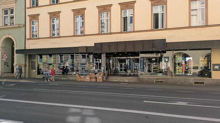 Die Fassade eines Titus-Shops in Bamberg. Passanten gehen vorbei, Kartons stehen vor dem Schaufenster, das mit Sale-Schildern dekoriert ist.