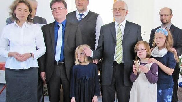 Bei der Segnung zur Amtseinführung von Pastor Sebastian Thierfelder wurden die Augen geschlossen (von links): Annett Thierfelder, Seniorpastor Bernd Heise (verdeckt), Pastor Sebastian Thierfelder, Leitungsratsmitglied Detlev Bilek, Thalitha Thierfelder, Gemeindeleiter Wolfgang Freigang, Salome und Deborah Thierfelder sowie Leitungsratsmitglied Ralf Seiler.  Foto: Martin Koch