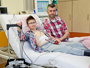 Mit einem Kunstherz liegt der 15-jährige Marc (l) neben seinem Vater Andre in der Kinderkardiologie am Uniklinikum Erlangen an der Dialyse. Der Jugendliche hat eine Kardiomyopathie, eine angeborene Herzmuskelschwäche und lebt nur noch dank eines Kunstherzens. Seit es nach einem Eingriff schwere Komplikationen gab, funktionieren auch seine Nieren nicht mehr richtig. Dreimal in der Woche muss er fünf Stunden lang ins Krankenhaus zur Dialyse. Foto: Daniel Karmann/dpa