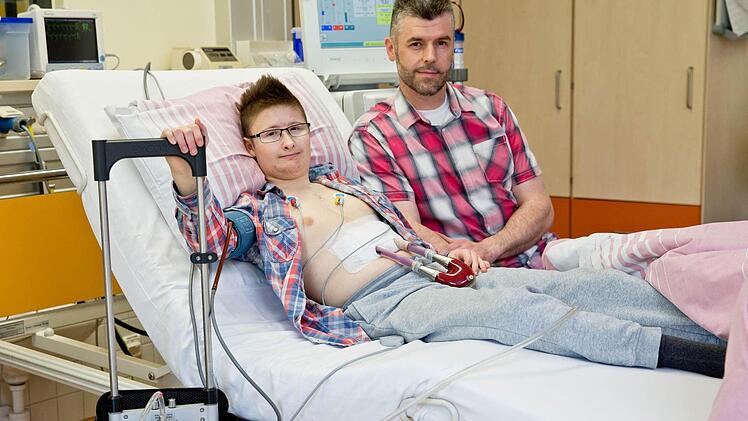 Mit einem Kunstherz liegt der 15-jährige Marc (l) neben seinem Vater Andre in der Kinderkardiologie am Uniklinikum Erlangen an der Dialyse. Der Jugendliche hat eine Kardiomyopathie, eine angeborene Herzmuskelschwäche und lebt nur noch dank eines Kunstherzens. Seit es nach einem Eingriff schwere Komplikationen gab, funktionieren auch seine Nieren nicht mehr richtig. Dreimal in der Woche muss er fünf Stunden lang ins Krankenhaus zur Dialyse. Foto: Daniel Karmann/dpa