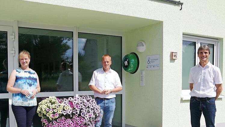 Projektleiterin Antje Angles, Bürgermeister Thomas Löffler sowie BRK-Kreisvorsitzender Roland Beierwaltes (von links) freuen sich über den am Mehrgenerationenhaus angebrachten Defibrillator. Foto: Heike Schülein