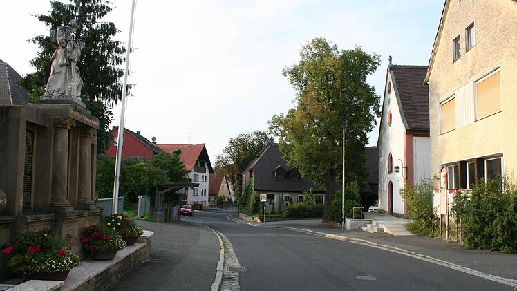 Die Ortsmitte heute: mit Kriegerdenkmal, Zugang zur ehemaligen Brauerei-Gaststätte und Bushaltestelle auf der einen, altem Schulhaus und Kirche auf der anderen Straßenseite