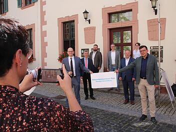 Gruppenbild von der offiziellen Eröffnung am Eingang zum Roten Schloss in Hammelburg: Der Bad Kissinger OB Dirk Vogel (links) und der Hammelburger Bürgermeister Armin Warmuth (rechts) halten das neue NEZ-Schild. Dahinter Abteilungsdirektor Bertram Eidel und Landrat Thomas Bold, auf der Treppe die Mitarbeiter Felix Papsch, Dr. Joachim Schneider und Lisa Graskamp. Foto: Ralf Ruppert