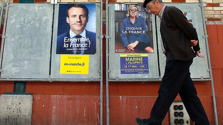 Ein Mann geht in Saint-Jean-de-Luz (Frankreich) an Wahlplakaten des sozialliberalen Präsidentschaftskandidaten Emmanuel Macron (l) und der rechtspopulistischen Präsidentschaftskandidaten Marine Le Pen vorüber. Die Franzosen wählen am 07. Mai in einer Stichwahl ihr neues Staatsoberhaupt. Foto: Bob Edme/AP/dpa