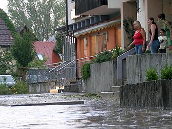 Anwohner schauen auf eine überflutete Straße in Neunkirchen am Brand. Foto: News5 / Herse