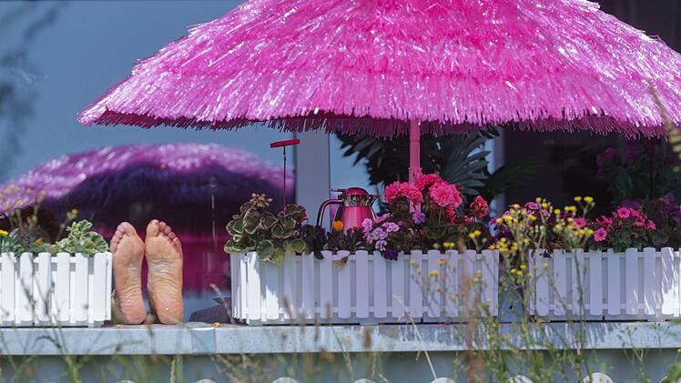Frau liegt auf einem Balkon unter einem pinken Sonnenschirm