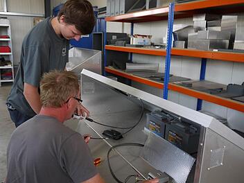 Lothar Seifert und sein Sohn Andre installieren die elektrischen Anschlüsse in dem Gerät, in dessen Inneren zwei große Akku-Blöcke den Stromspeichern, den das Photovoltaik-Modul tagsüber erzeugt. Foto: Pauline Lindner