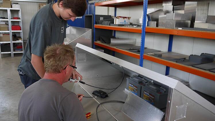 Lothar Seifert und sein Sohn Andre installieren die elektrischen Anschlüsse in dem Gerät, in dessen Inneren zwei große Akku-Blöcke den Stromspeichern, den das Photovoltaik-Modul tagsüber erzeugt. Foto: Pauline Lindner