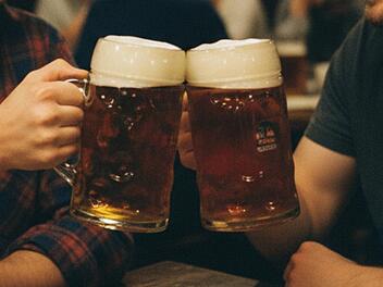 Zwei Kumpels um die 30 stoßen mit 0,5-Liter Krügen voller Bockbier an.