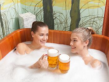 Beautiful girl enjoying a beer bath. Young women relaxing in the beer spa. Bathing in beer. (color toned image). Beautiful women in a beer spa.
