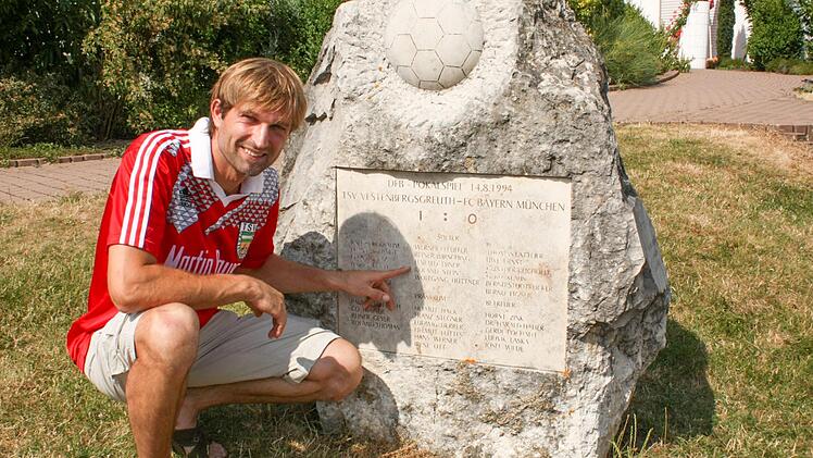 Roland Steins Name ist auf dem 1:0-Gedenkstein vor dem Sportheim in Vestenbergsgreuth verewigt. Fürs Foto hat er noch einmal sein altes Trikot übergestreift. Foto: Archiv