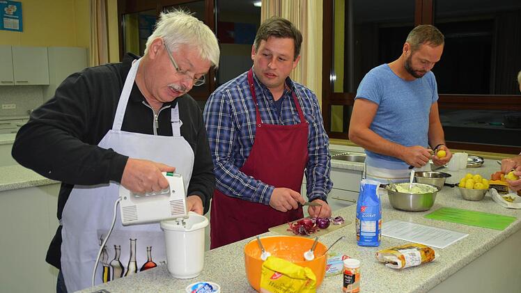 Helmut Schneider rührt Sahne für die Nachspeise, während sein Sohn Michael Zwiebeln schneidet. Rechts pellt Michael Hauck Kartoffeln. Foto: Kathrin Kupka-Hahn