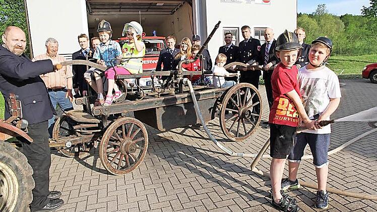 Mitglieder der Wehr, der Feuerwehrnachwuchs und der Schirmherr der Feierlichkeiten, Bürgermeister Claus Schwarzmann, präsentieren die alte Handspritzpumpe.  Foto: Mathias Erlwein