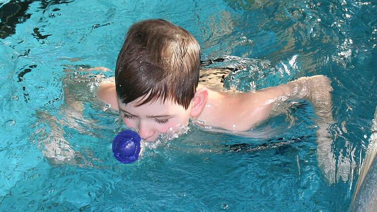Jonathan pustet einen Plastikball von einem Beckenrand zum anderen .